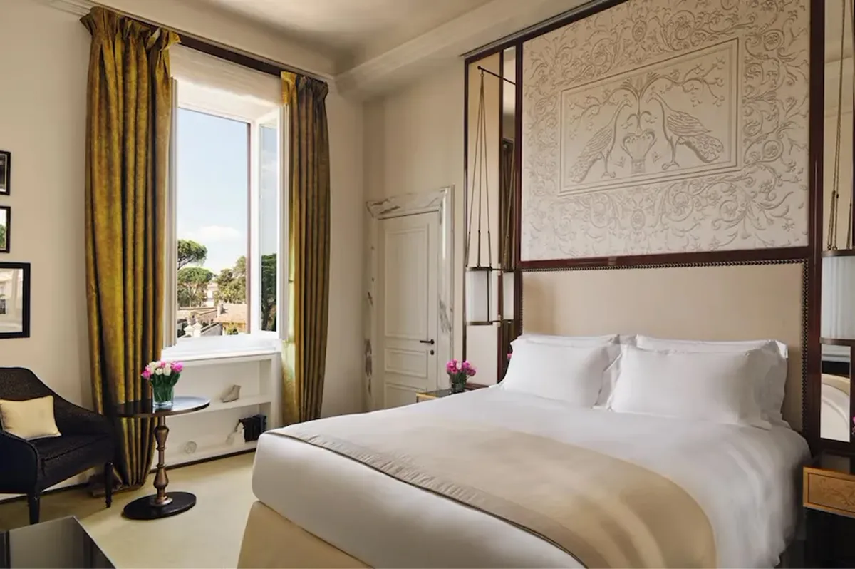 A bedroom with a four-poster canopy bed, window with gold drapes, and pale stone textured walls