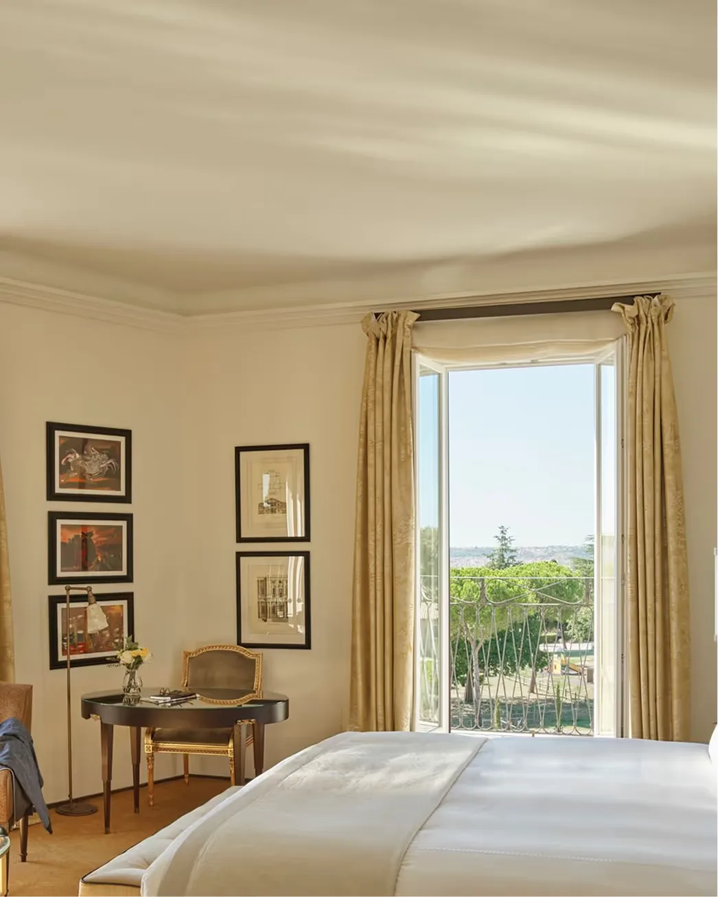 A bedroom with a canopy bed, dark wood frame, gold curtains, and framed artworks on the wall