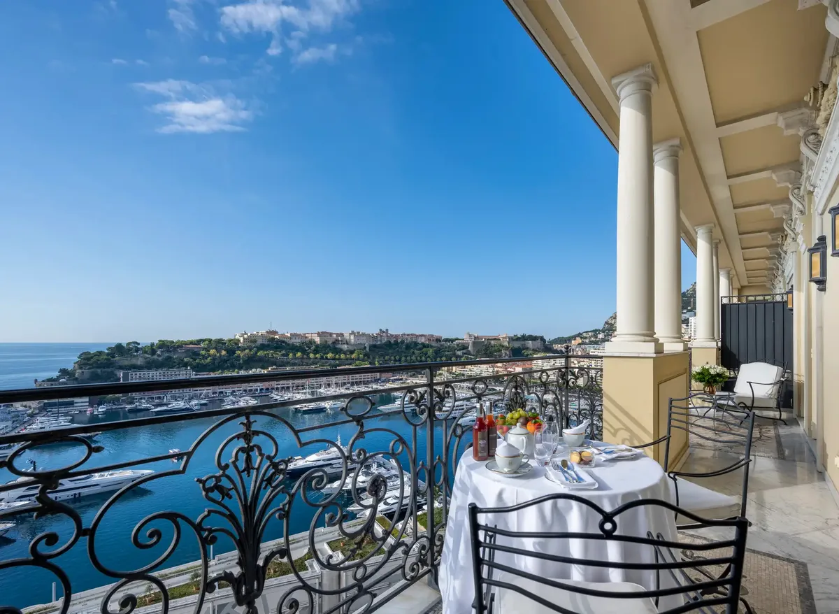 Wrought-iron terrace railing with sea and coastal buildings visible under blue sky