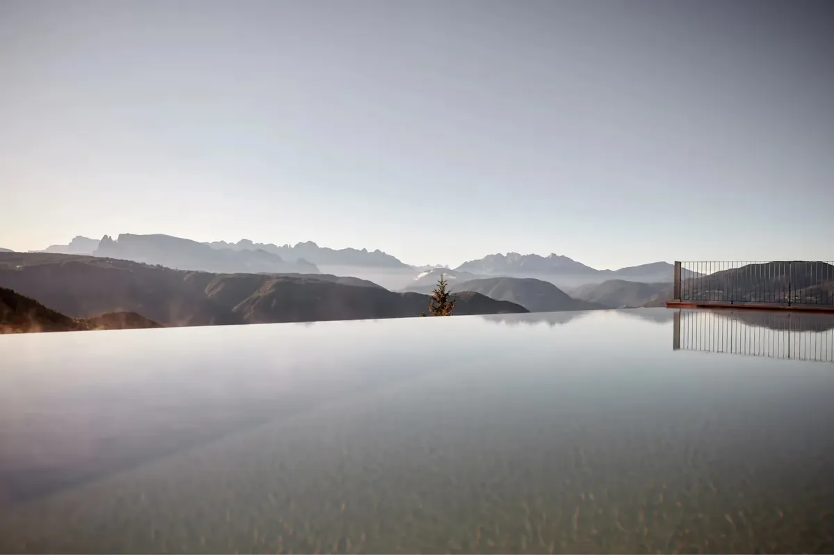 Reflection pool at sunrise with distant mountains and sparse trees in soft golden light
