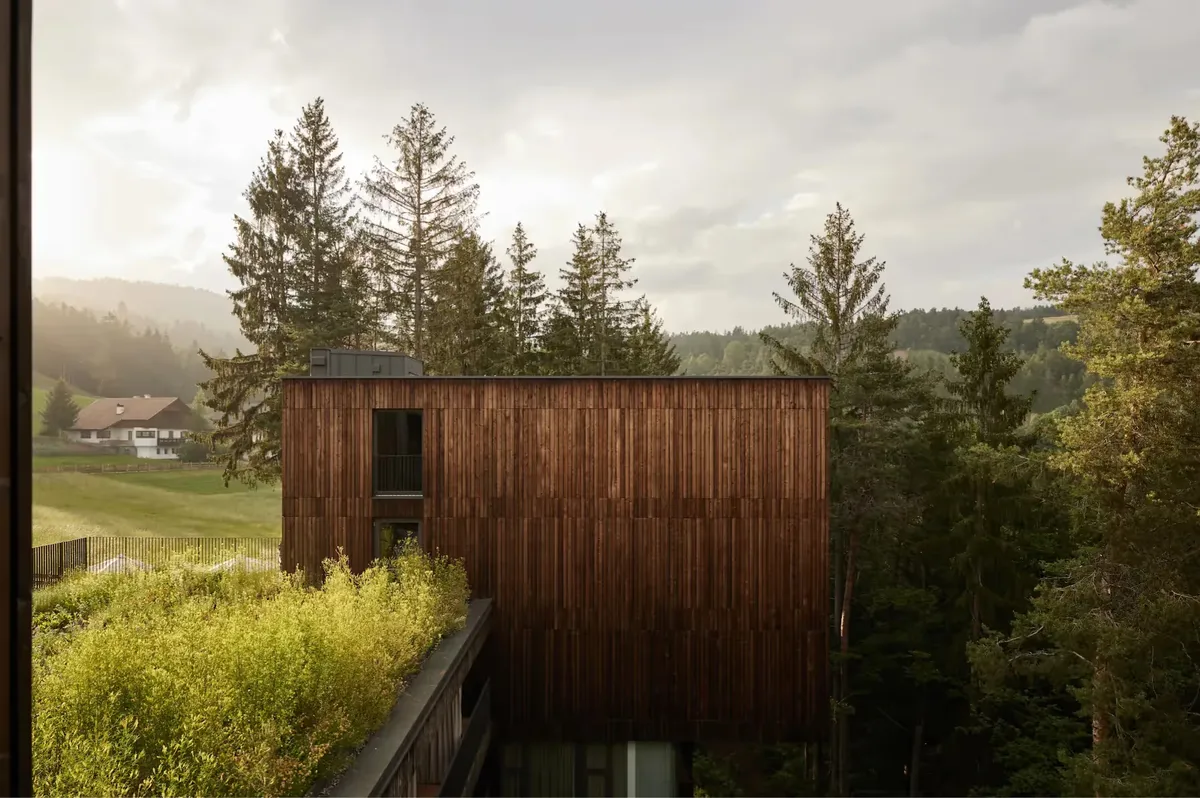 Dark wood building with windows set on hillside overlooking pastoral valley landscape