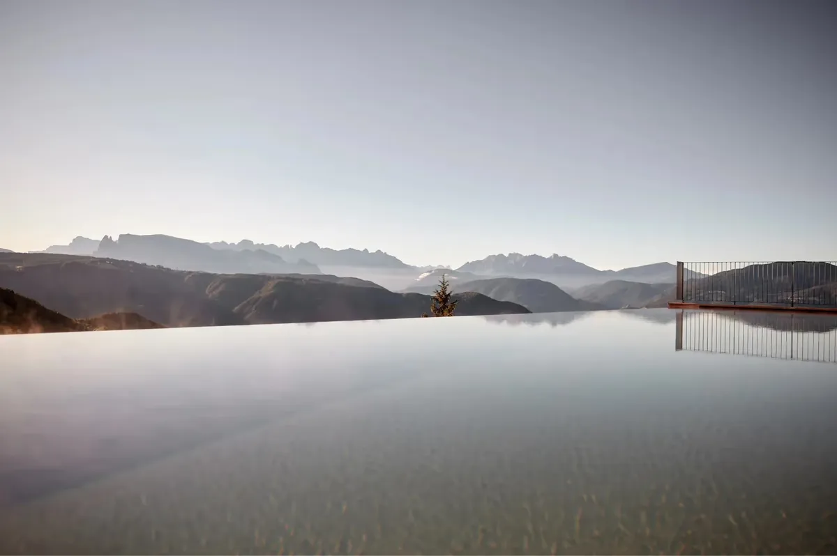 Infinity pool reflecting mountains at dawn in misty atmospheric light