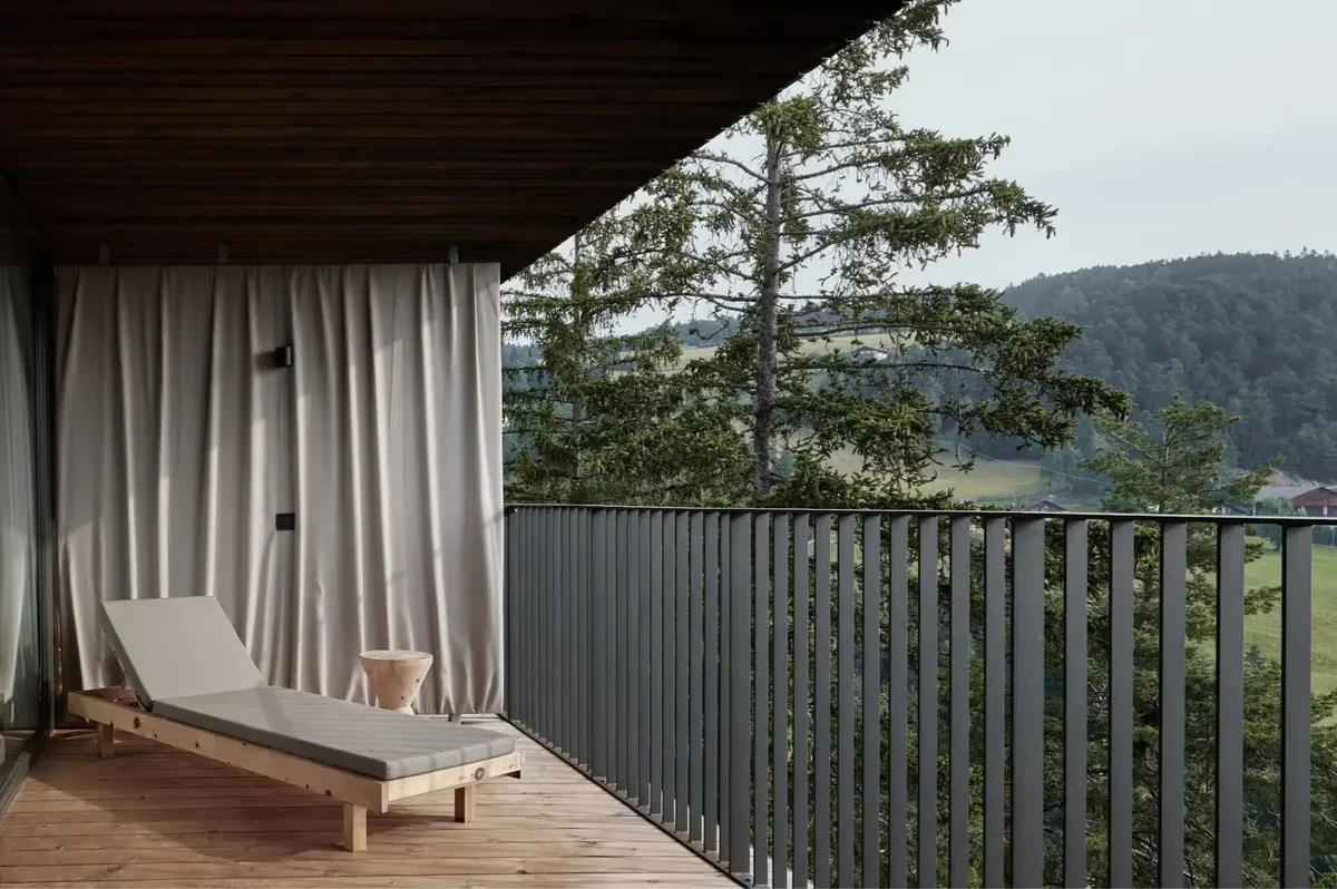 Covered wooden terrace with sheer curtains framing views of pine forest and distant mountains