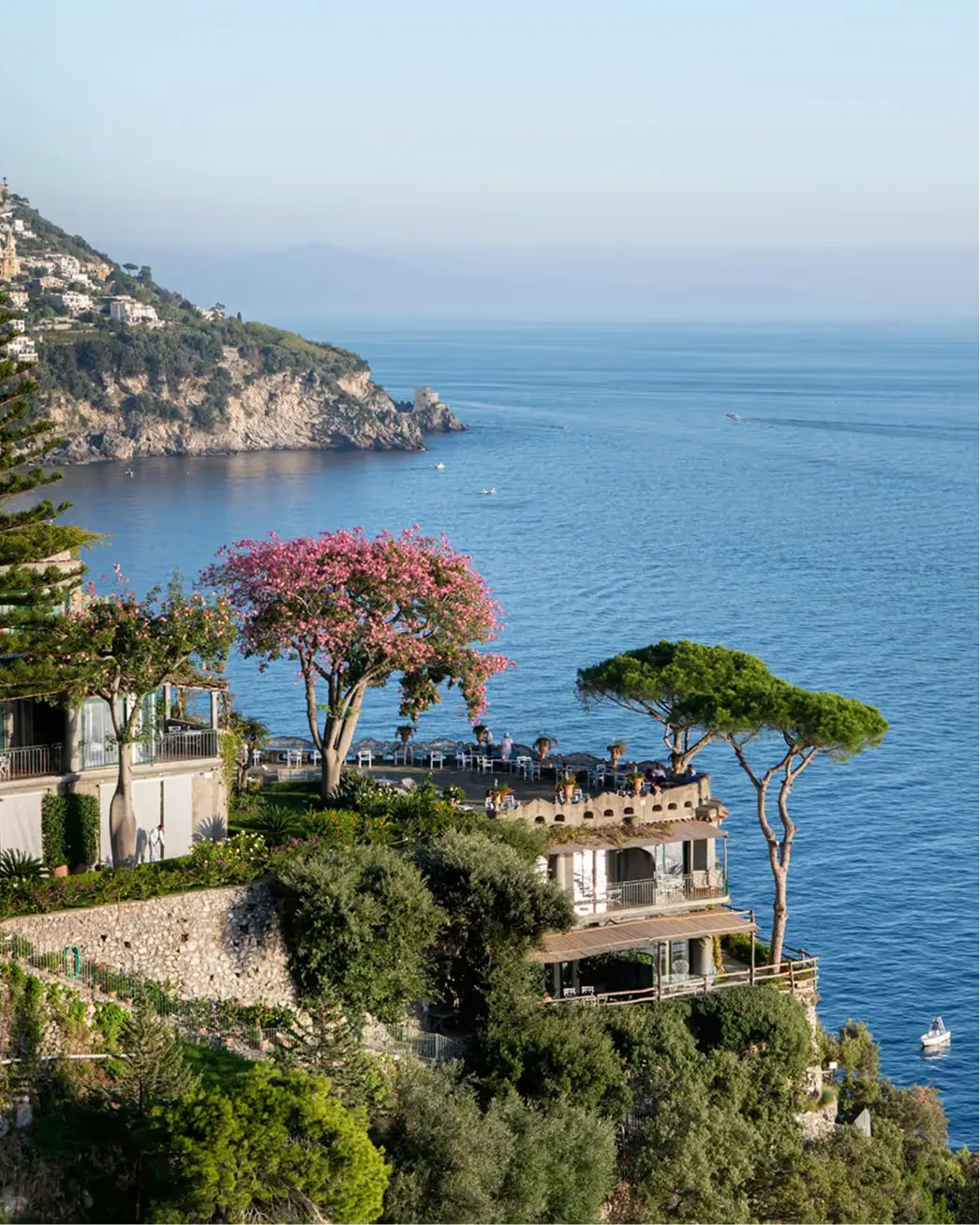 Stone hotel buildings on a Positano cliff with flowering magenta bougainvillea and sea beyond