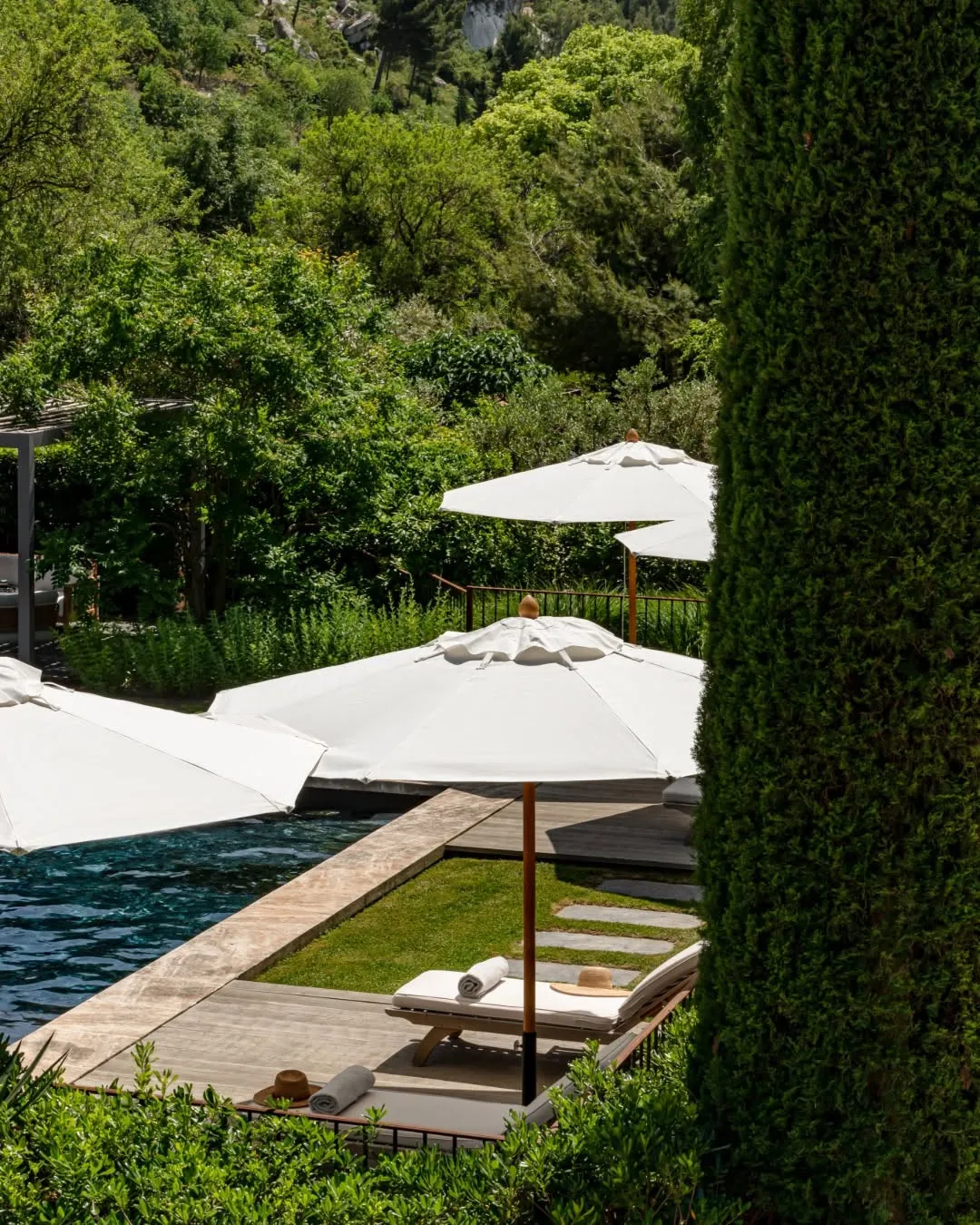 Hillside lounge terrace with tiered white shade sails, wooden loungers, cypress screens, valley horizon