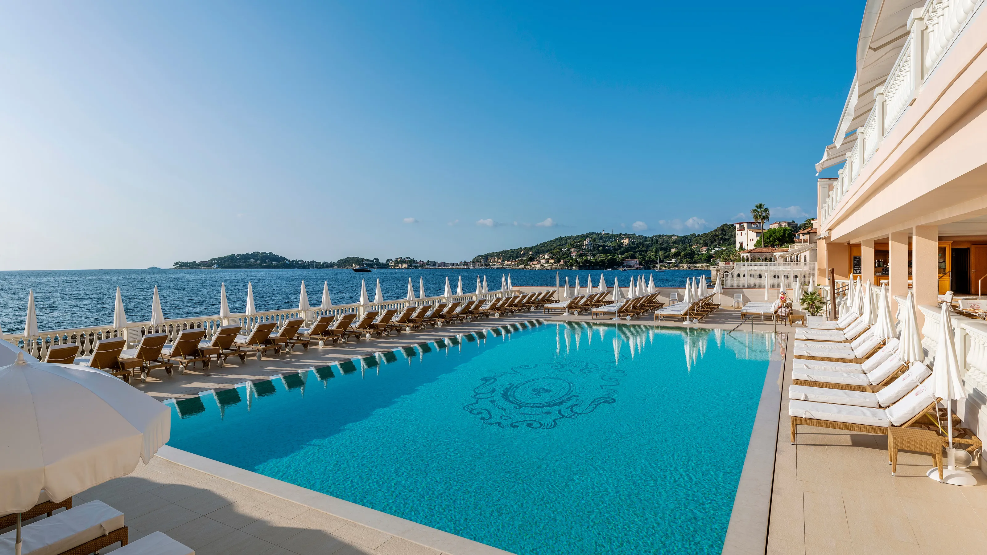 Heated seawater pool lined with white loungers overlooking the Mediterranean