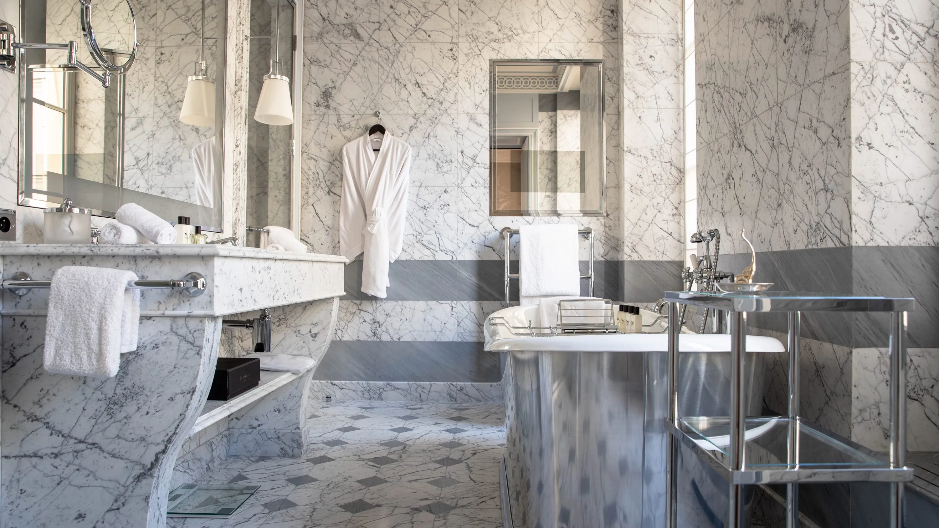 A marble bathroom with white and gray tones, featuring brass fixtures and a stone sink