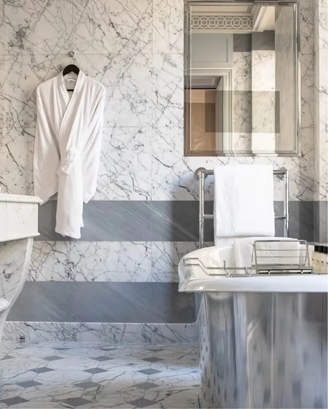 A marble bathroom with a plush white robe and brass mirror fixture