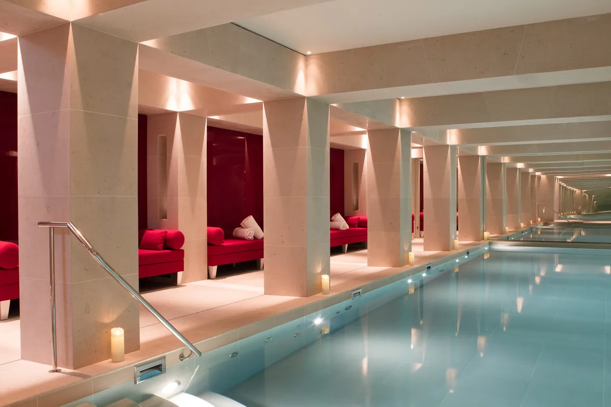 An indoor pool with red velvet seating alcoves and symmetrical warm lighting