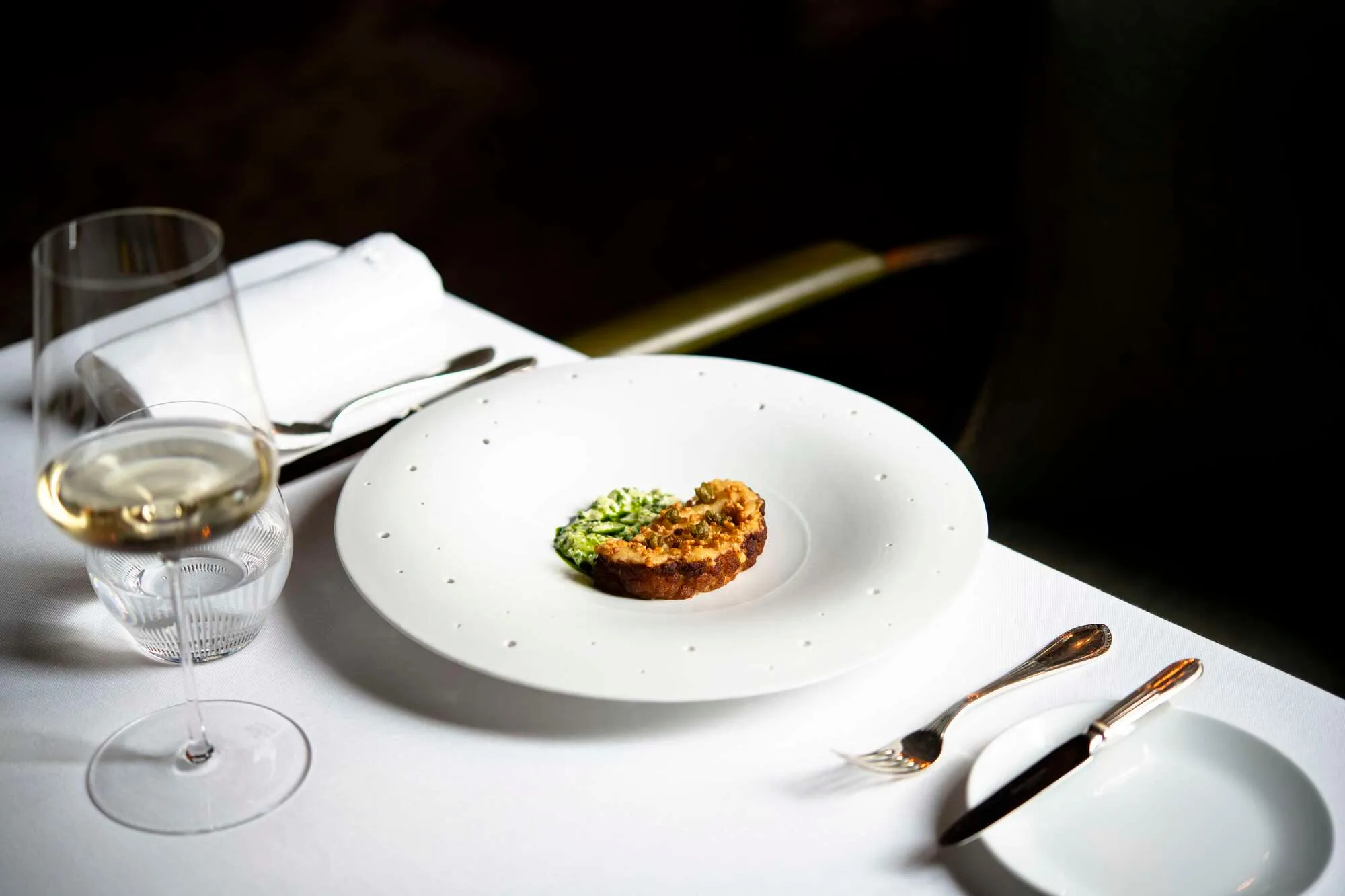 A fine dining plate with wine glass and formal place setting