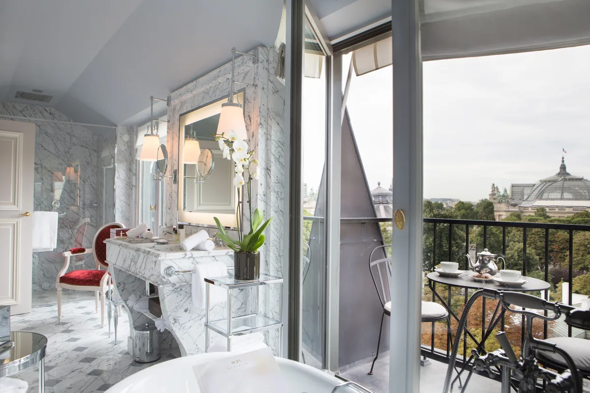 A bathroom with white marble, a red accent wall, and a mirrored vanity with Paris rooftop views