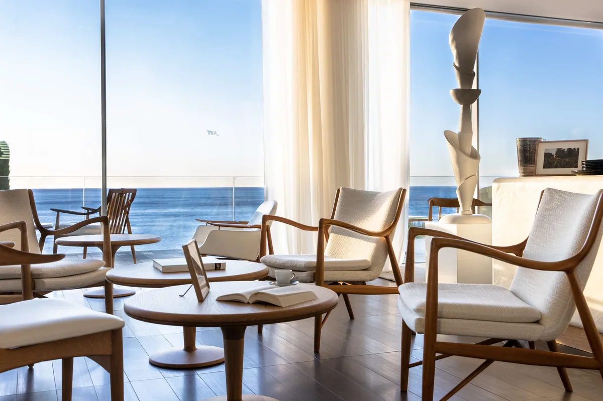 Light-filled lounge with woven chairs and sea views through glass doors