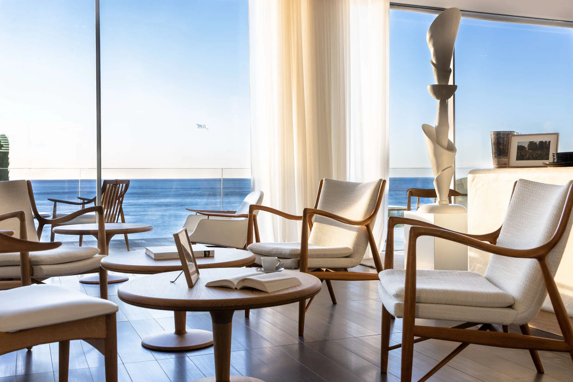 Light-filled lounge with woven chairs and sea views through glass doors