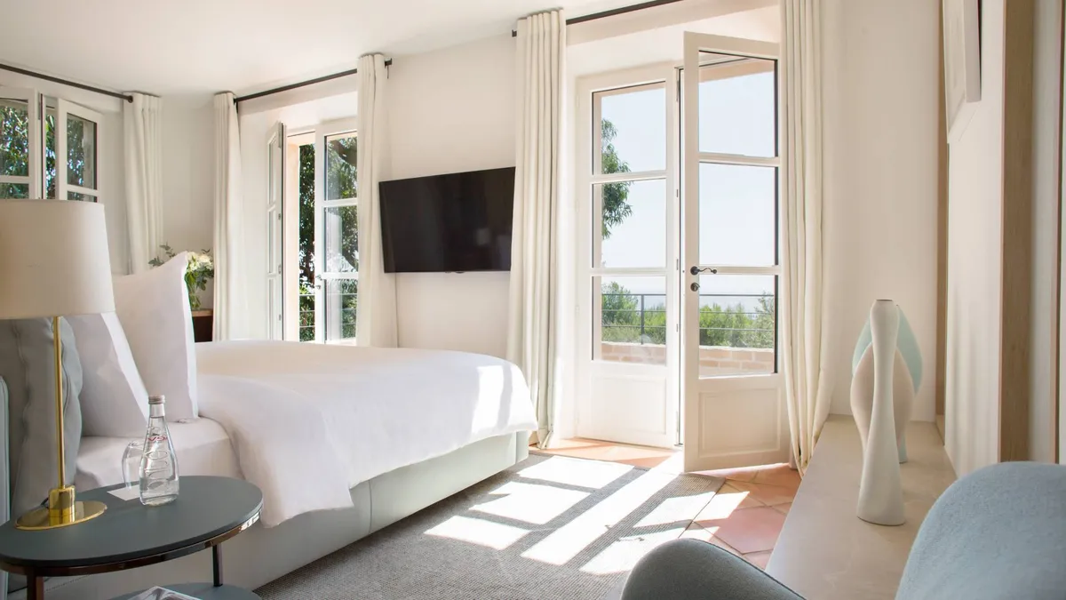 Bright bedroom with white bed and open doors to terraced seating