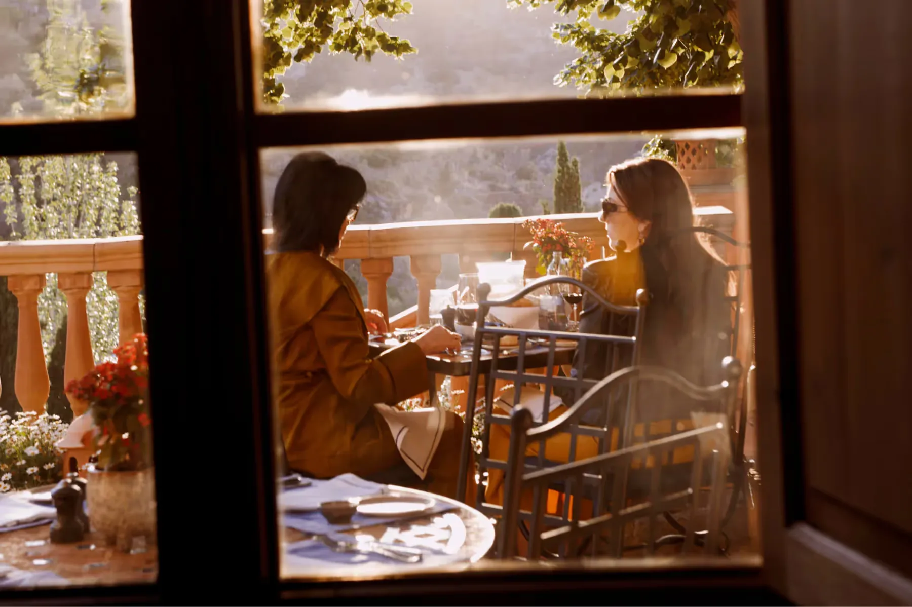 Two diners visible through window frame of restaurant with landscape view beyond