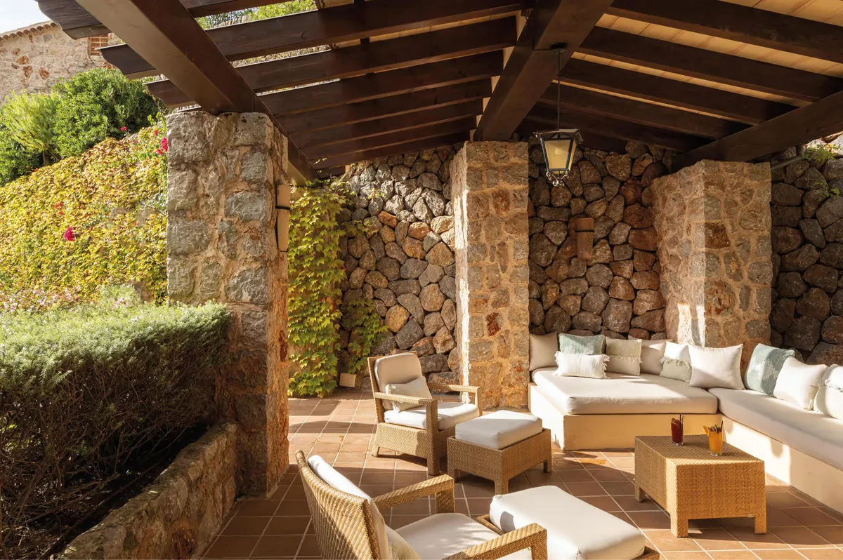 Covered patio with stone walls, wooden pergola, and cream-colored lounge seating