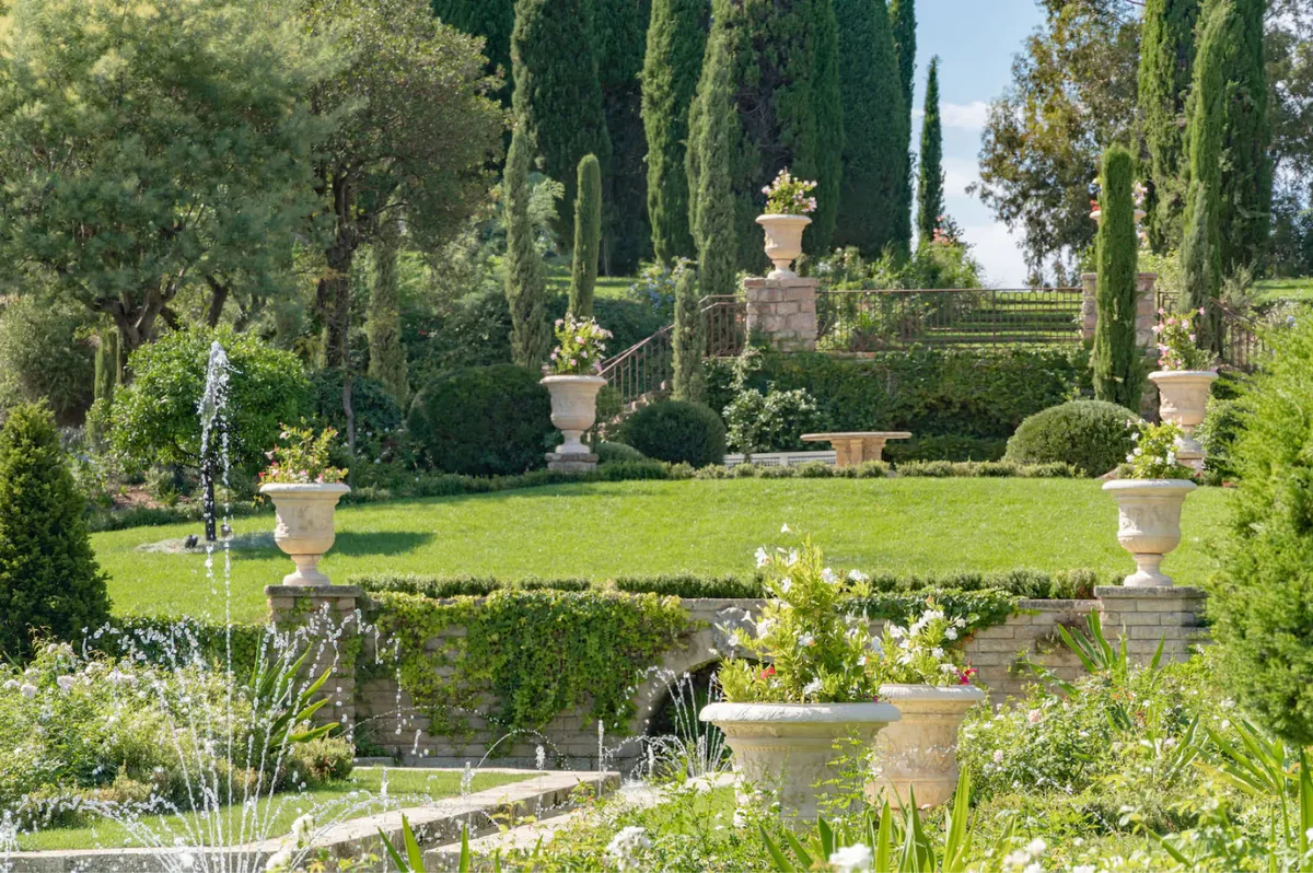 Terracotta urns and statuary on tiered garden beds with cypress groves and Mediterranean views