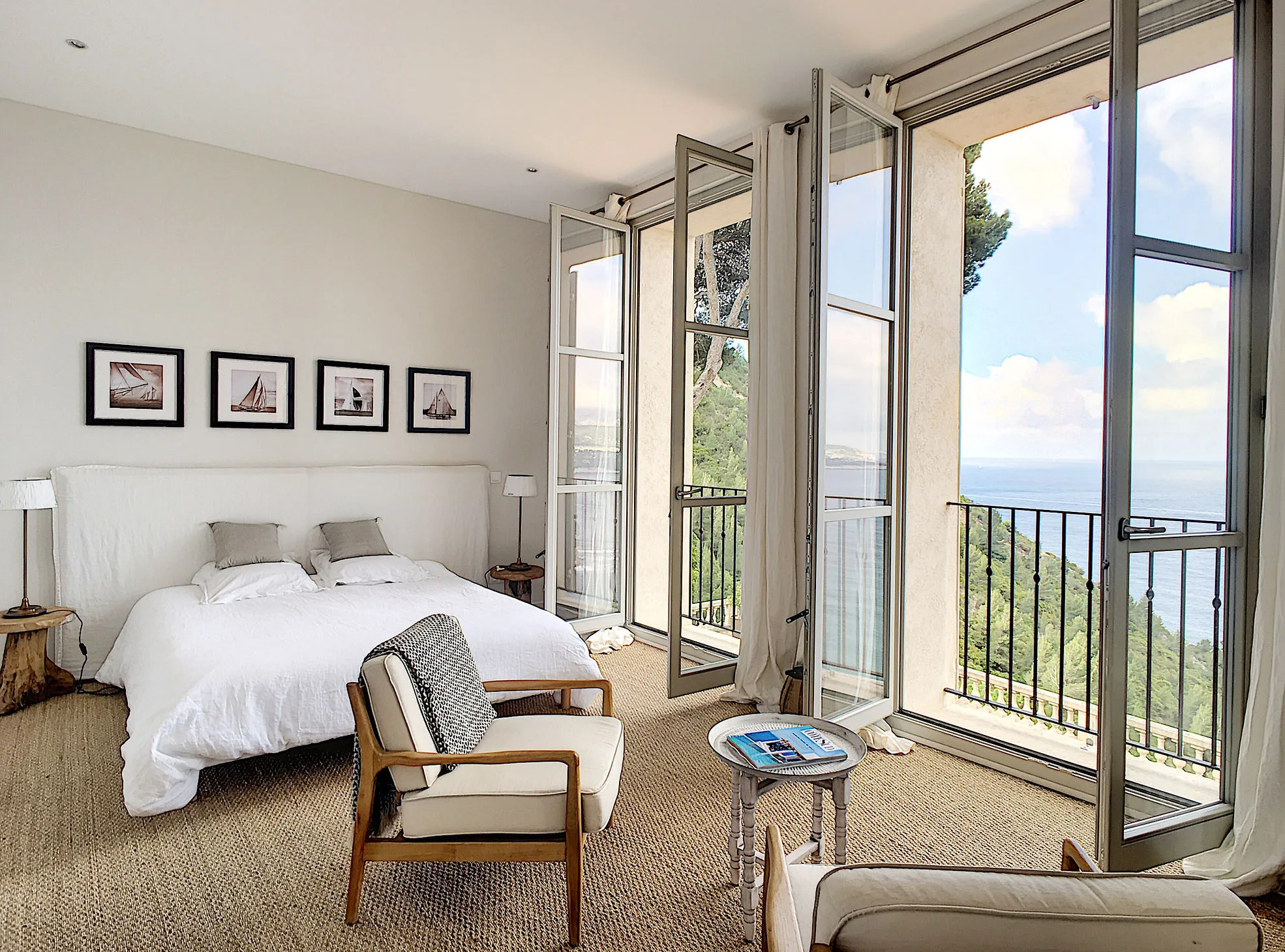 Sunlit bedroom with large glass doors opening to sea-view terrace and natural furnishings