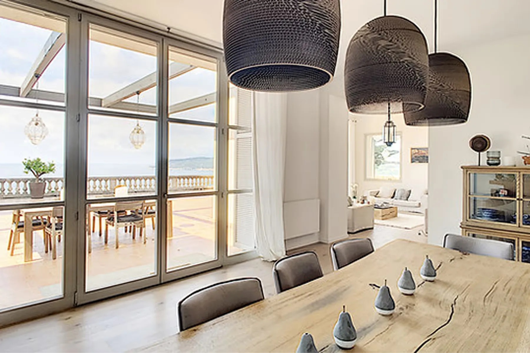 Dining room with beige walls, wooden table, and pendant light fixtures, coastal views beyond
