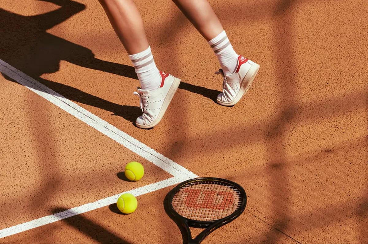 Tennis court with athletic shoes, racket, and bright yellow balls on rust-colored clay