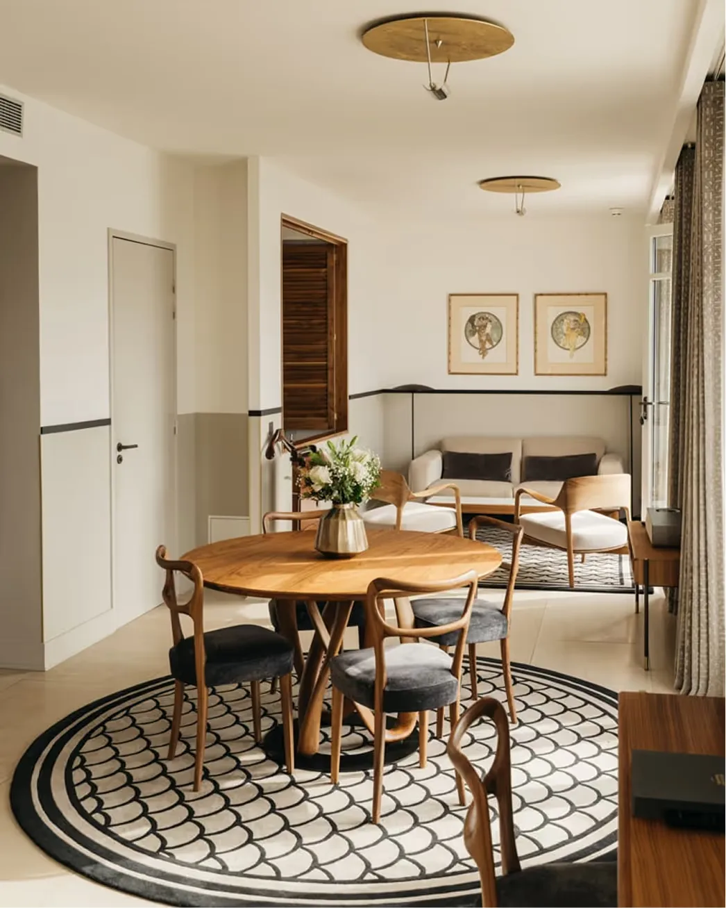 A dining space with wooden round table, rattan chairs, and botanical artwork on walls