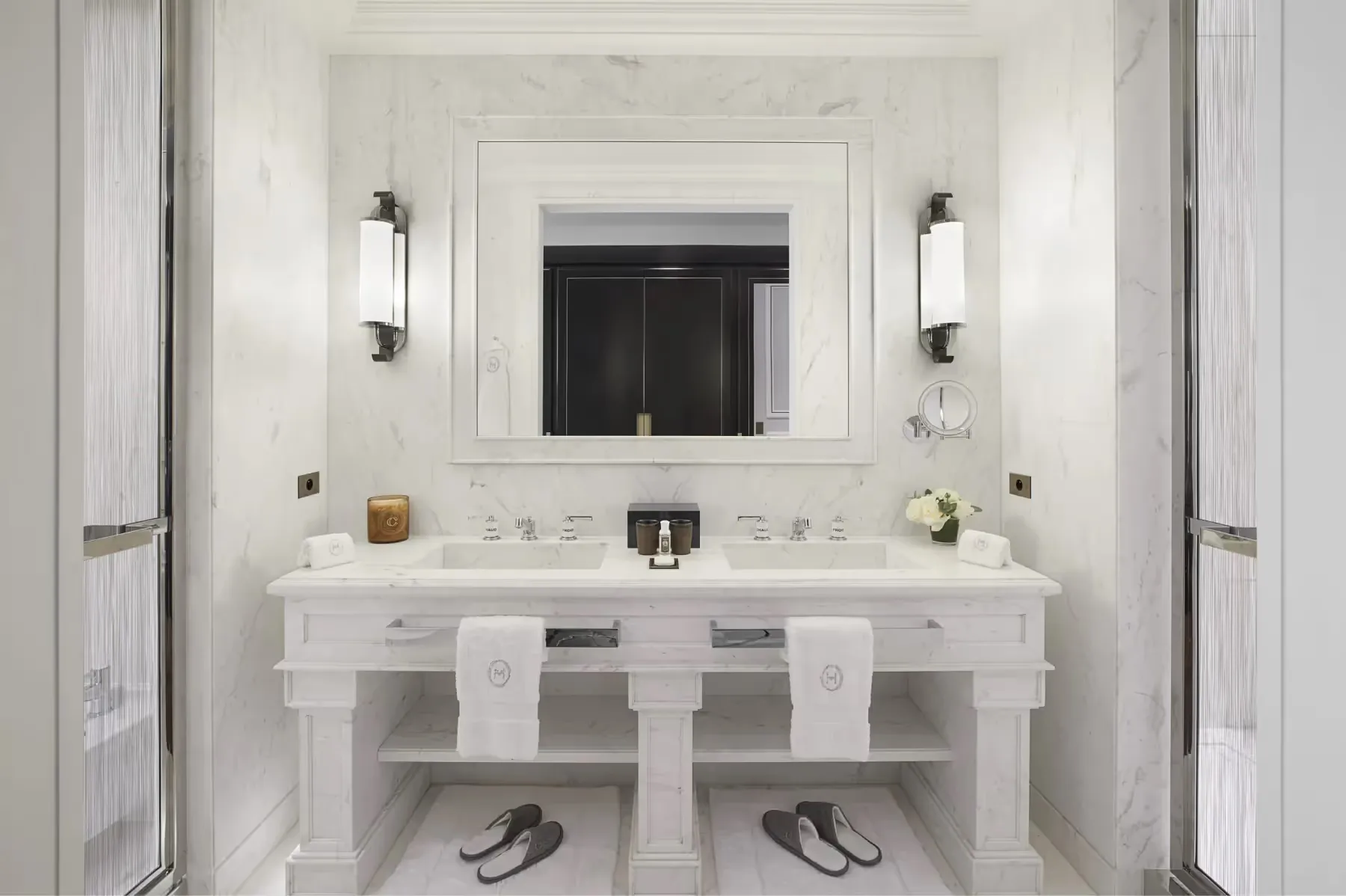 A marble bathroom with white twin vanities, large mirror, white sconces, and clean minimalist design