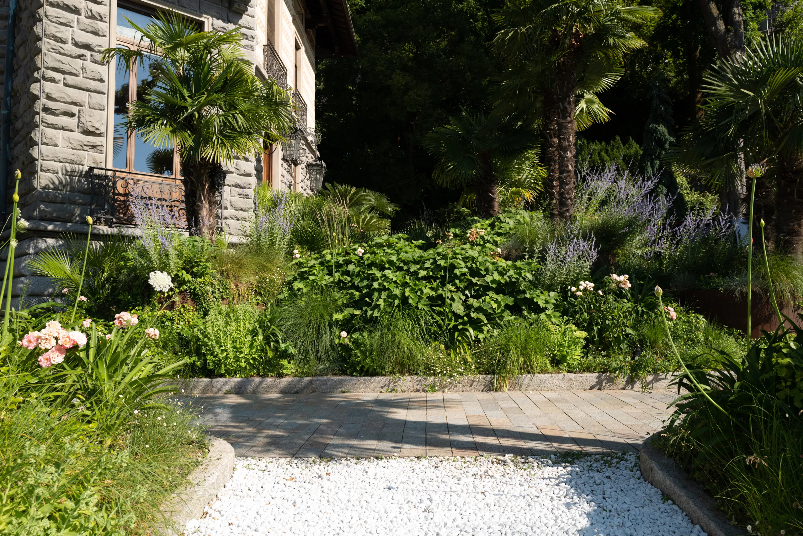 Shaded garden path with potted plants, flowering vines, and stone architecture