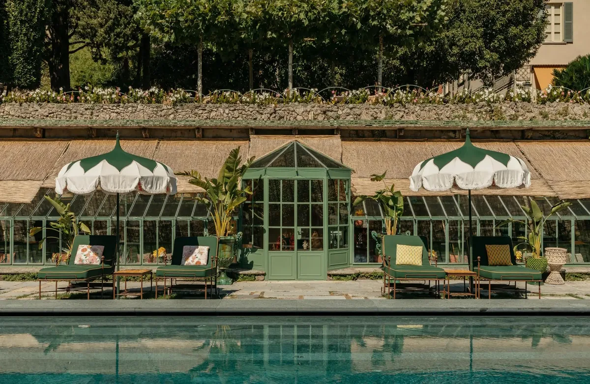 A stone terrace with loungers and white umbrellas beside a reflective pool