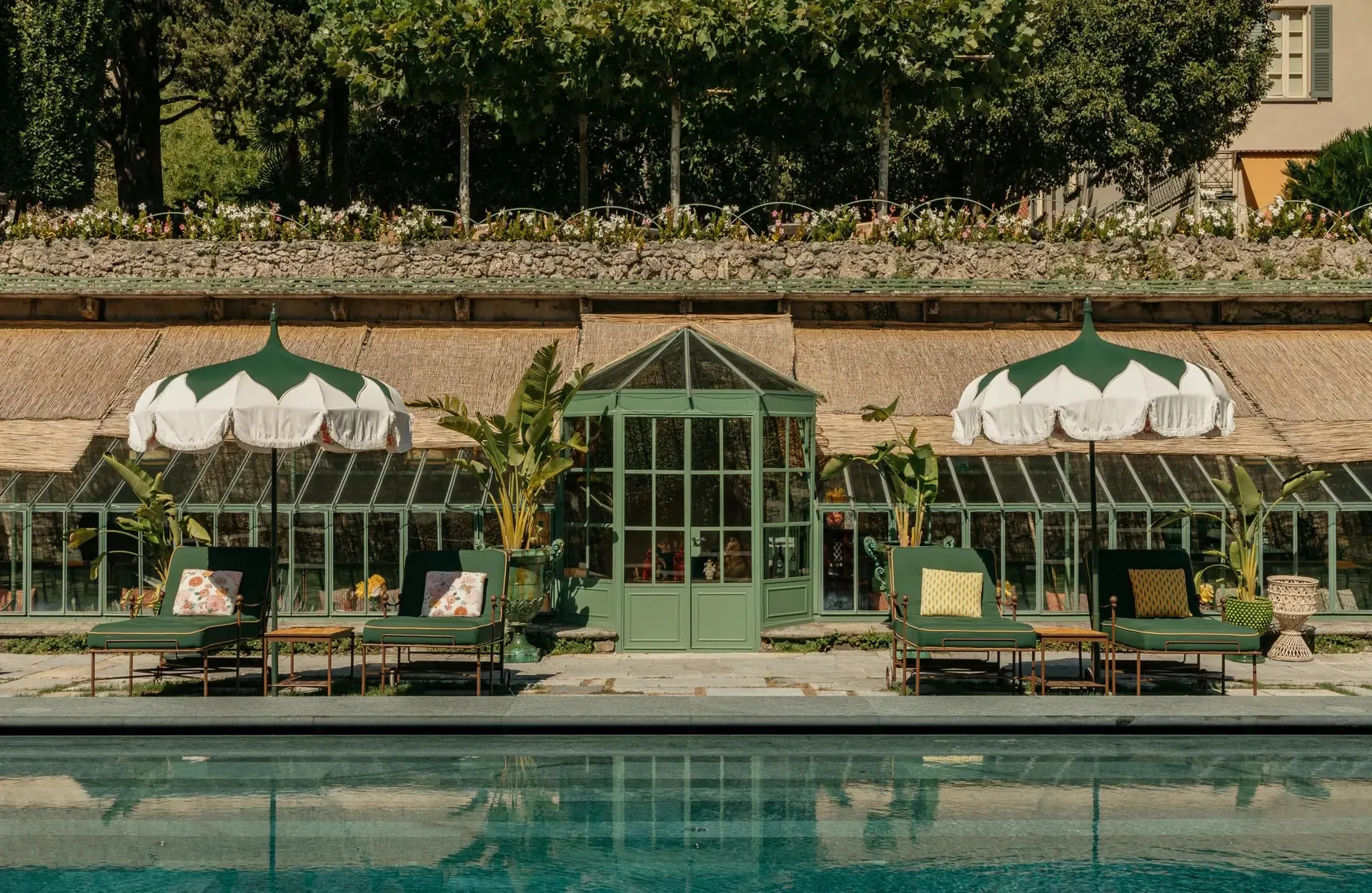 A stone terrace with loungers and white umbrellas beside a reflective pool