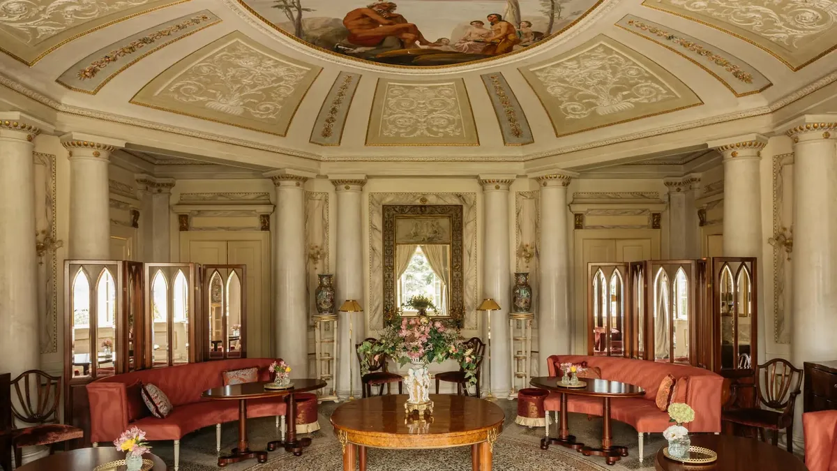 A cream-colored neoclassical salon with ornate ceiling, red velvet seating, and tall mirrors