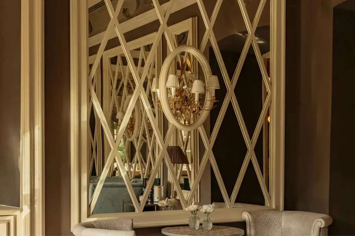 An ornate gold-framed mirror flanked by cream panels with geometric wallpaper