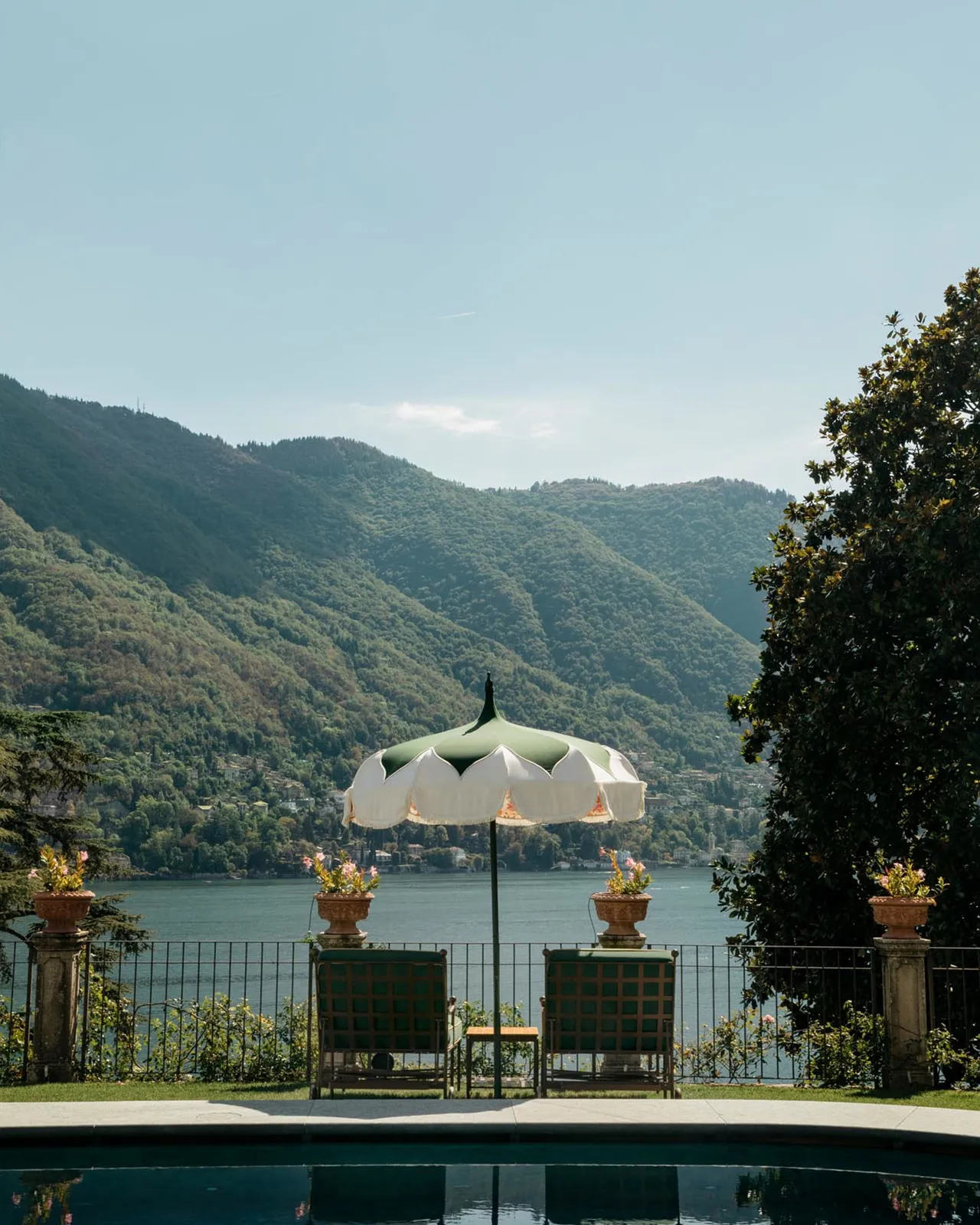 Cream umbrella with golden planters on a terrace above Lake Como’s turquoise water