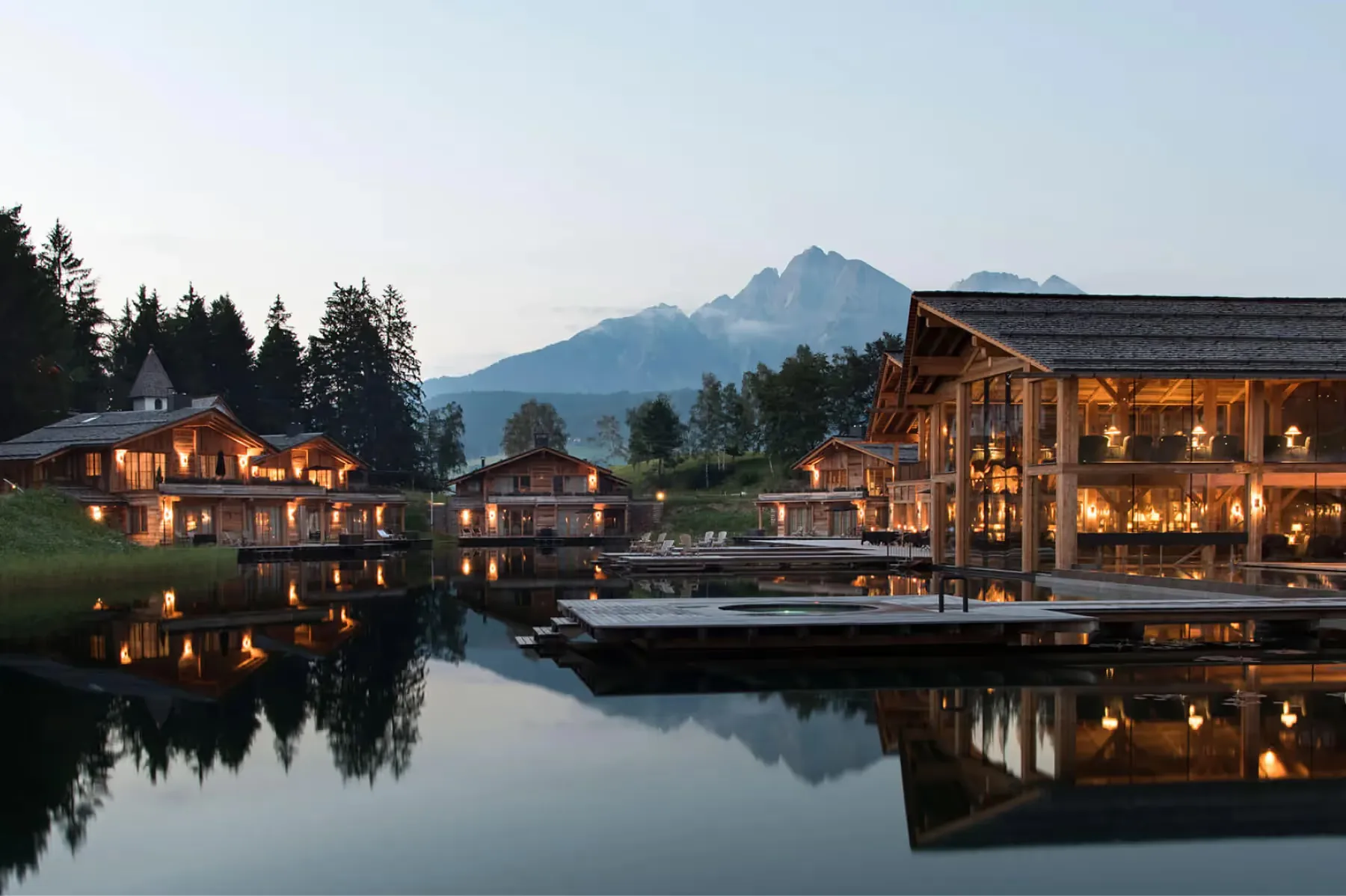 The hotel lit at dusk beside a reflective lake with mountains behind