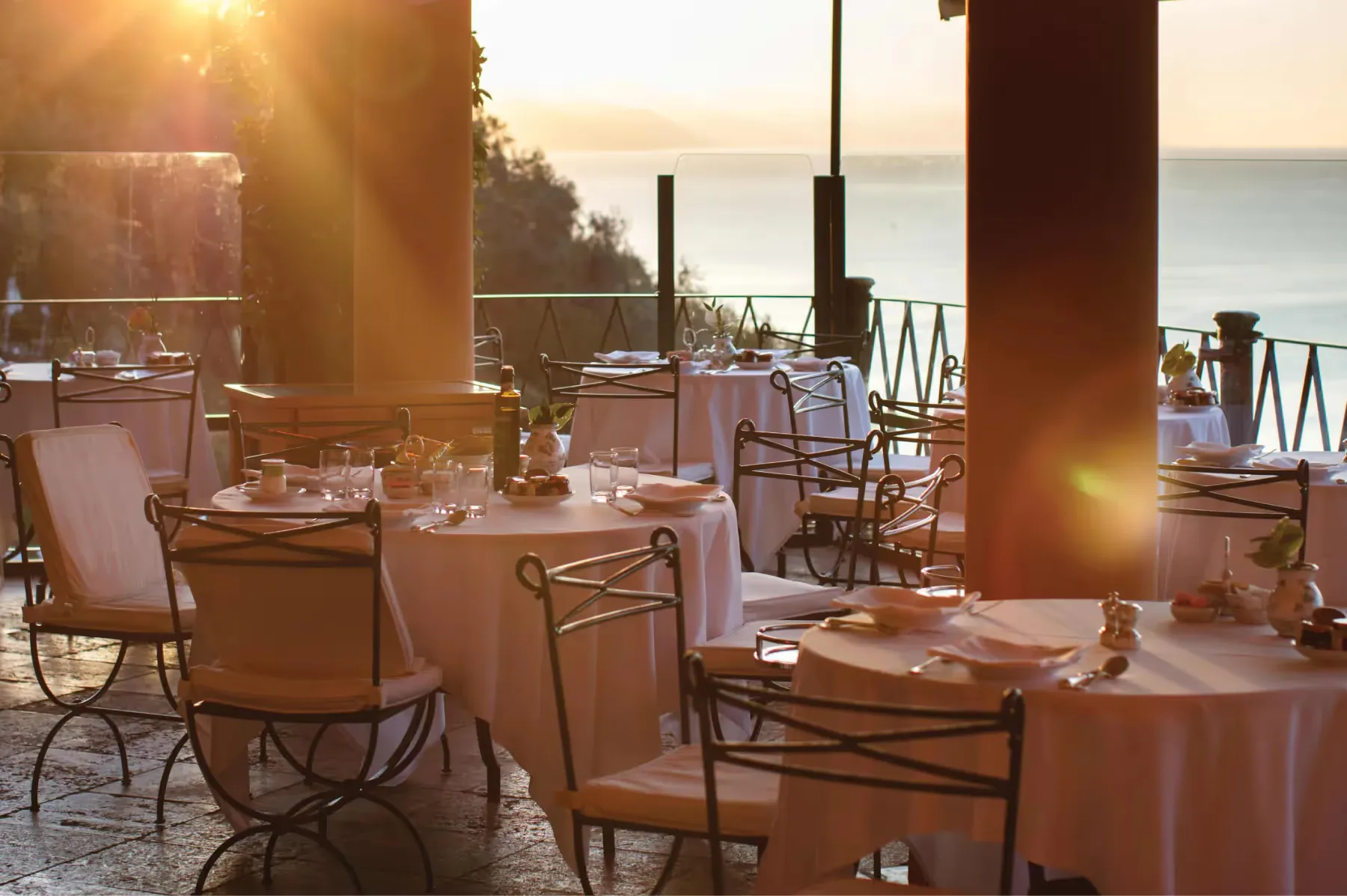 An elegant outdoor dining room with table settings and ocean view at sunset
