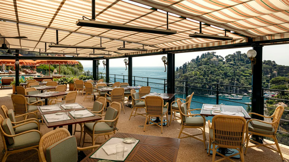 A sheltered dining pavilion with wood furnishings and turquoise harbor below