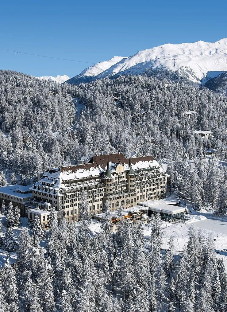 A grand Belle Époque hotel amid forested alpine slopes and mountain peaks in winter