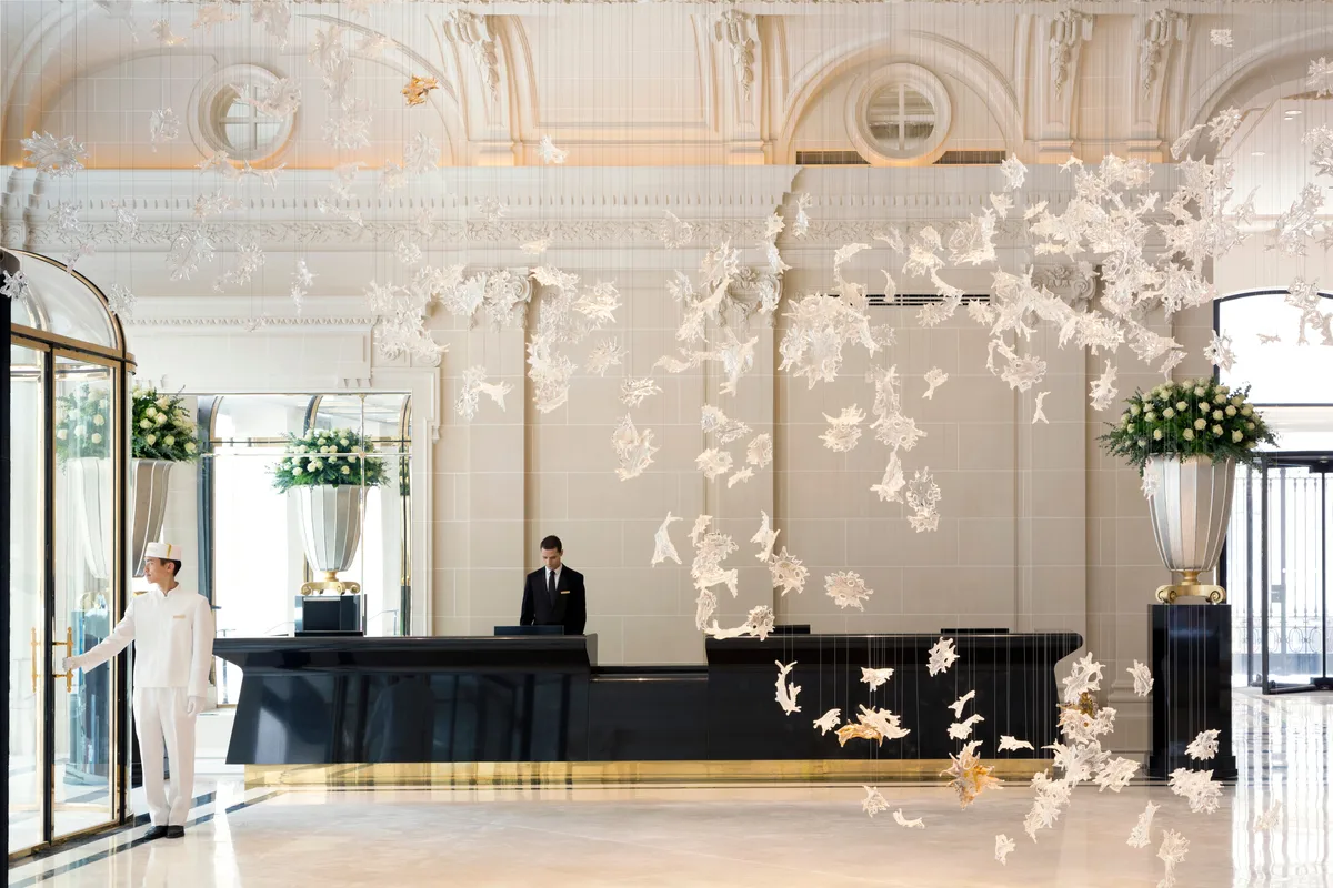 Grand lobby space with cream ceilings, gilded details, hanging installations, and a reception desk