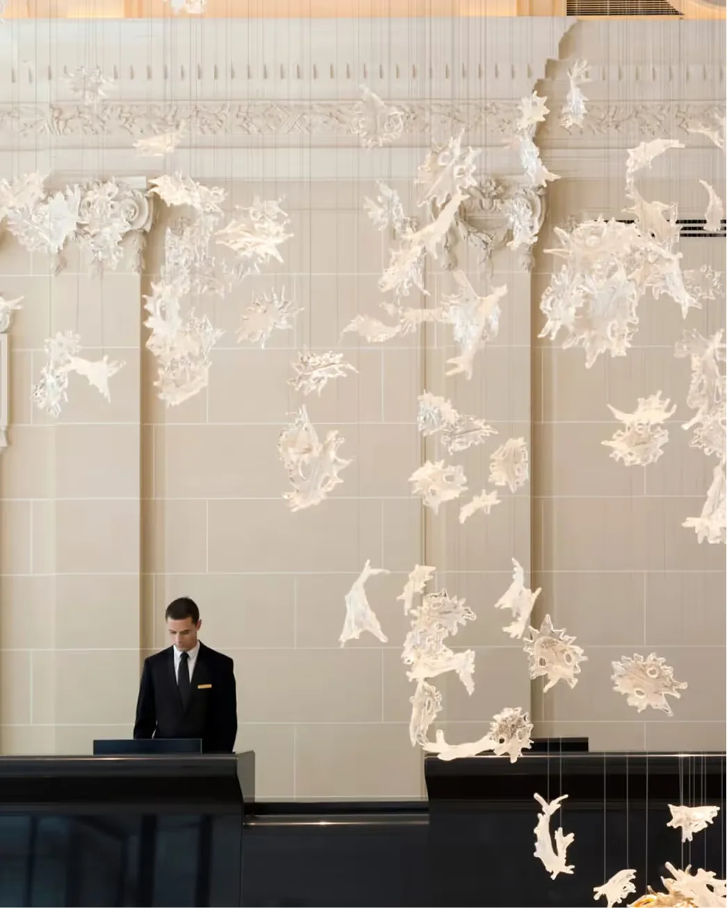 Cream walls with white floral silhouettes and a concierge in dark suit at a black desk