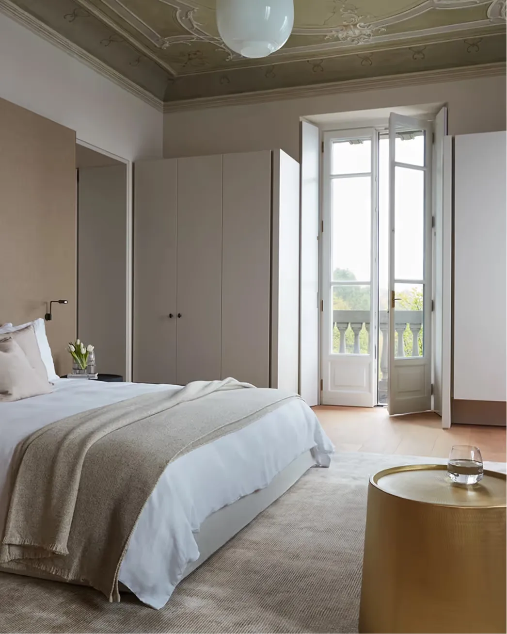 A bright suite with beamed ceiling, open doors to a balcony, and lake views beyond