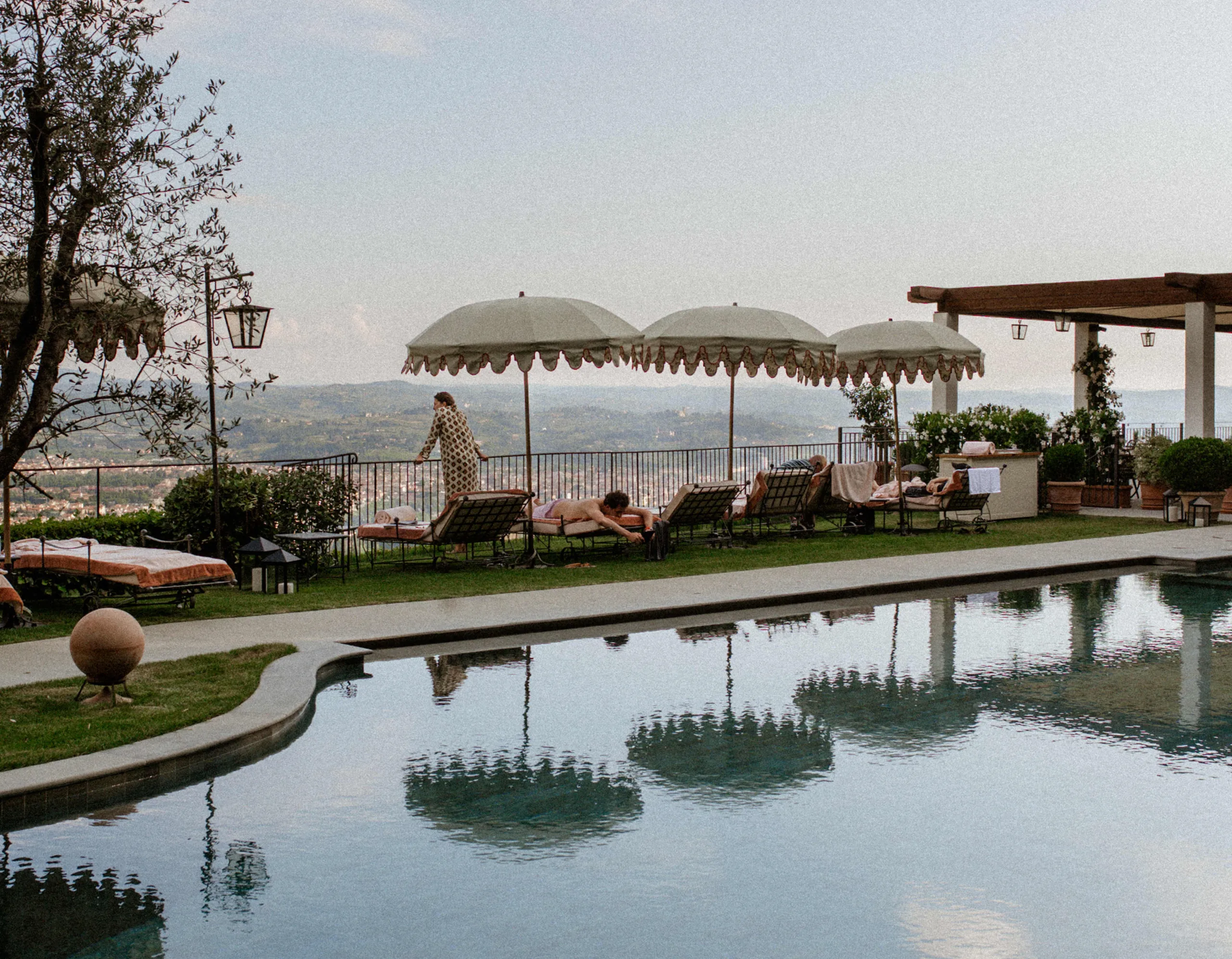 A swimming pool with cypress alleys, terrace seating, and Tuscan valley views beyond