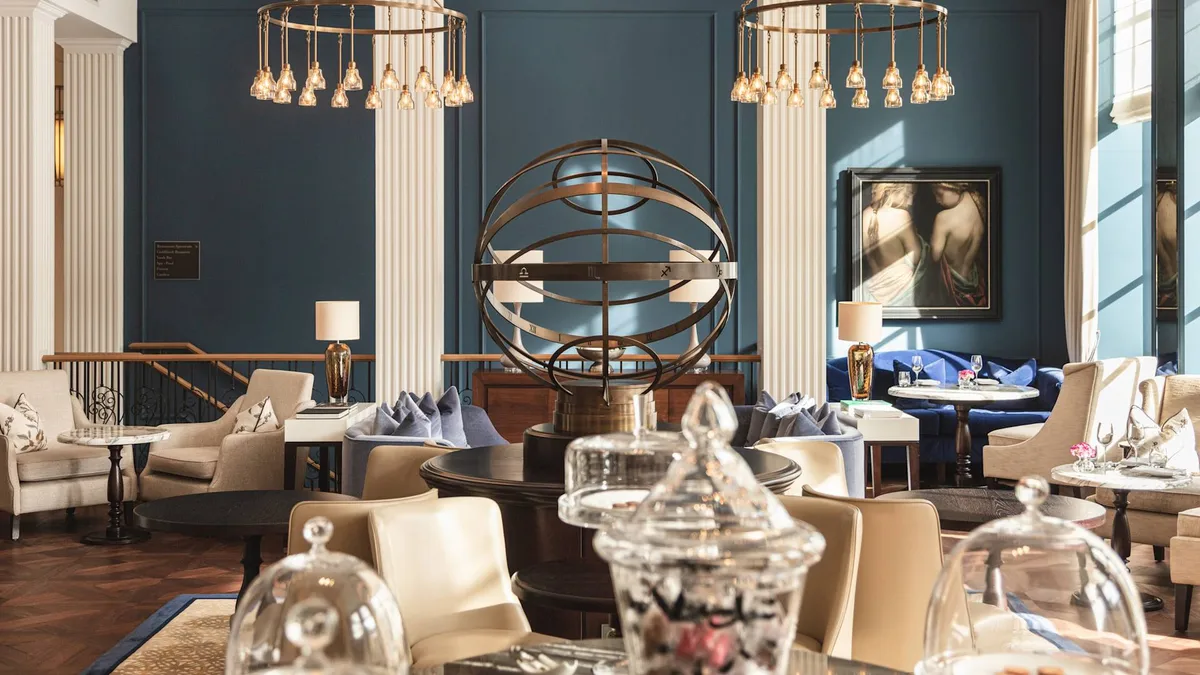 An elegant salon with blue walls, hanging gold light fixtures, marble columns, and modern sculptural art pieces
