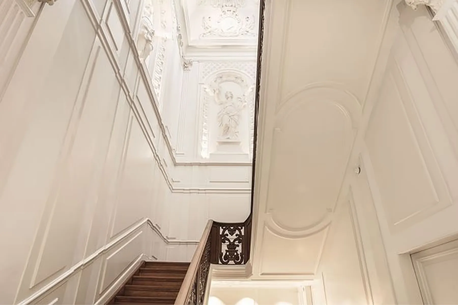 A stairwell with white paneled walls, arched skylight, and elegant railings creating a bright ascent